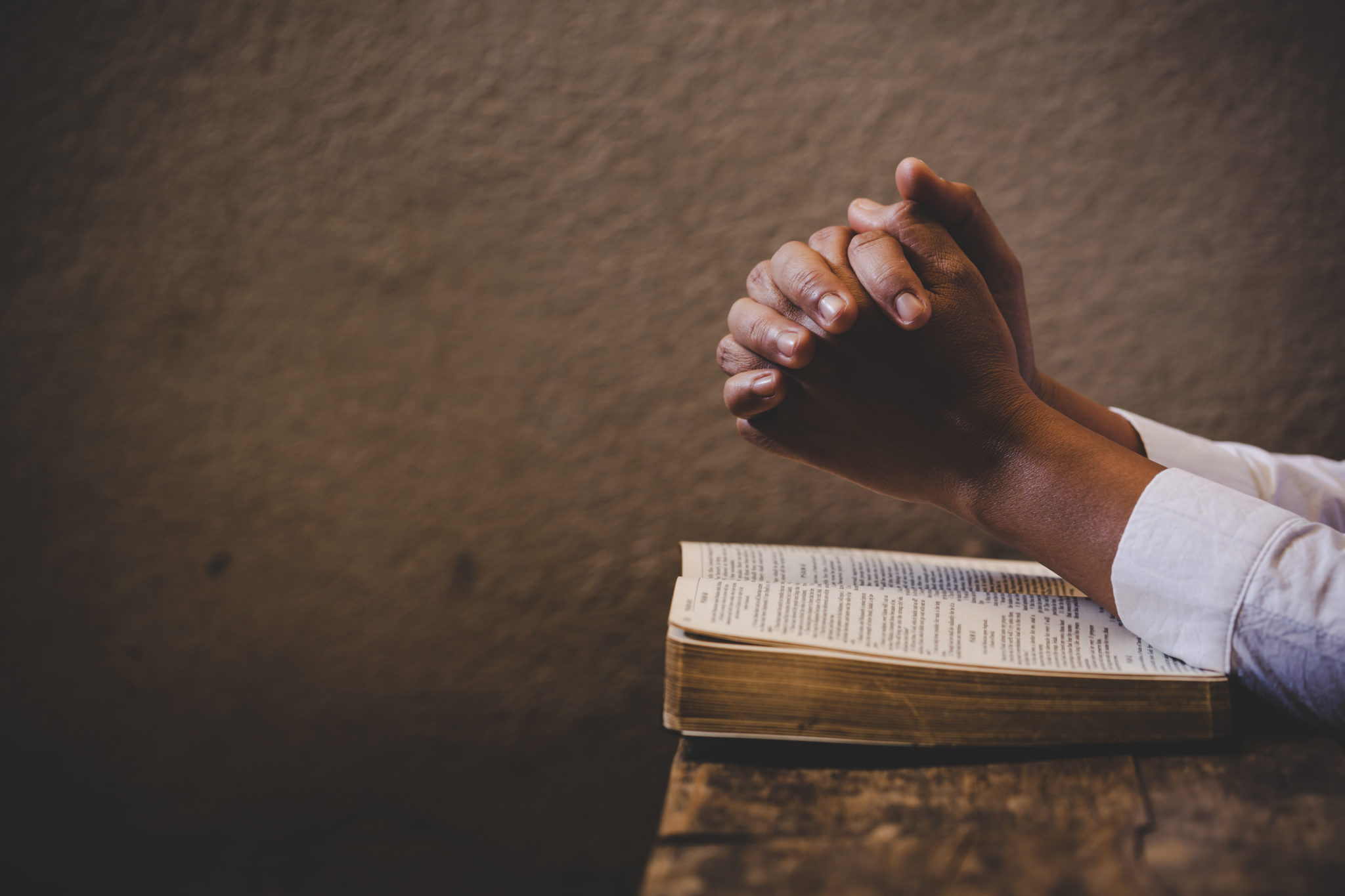 Hands folded in prayer on a Holy Bible in church concept for faith